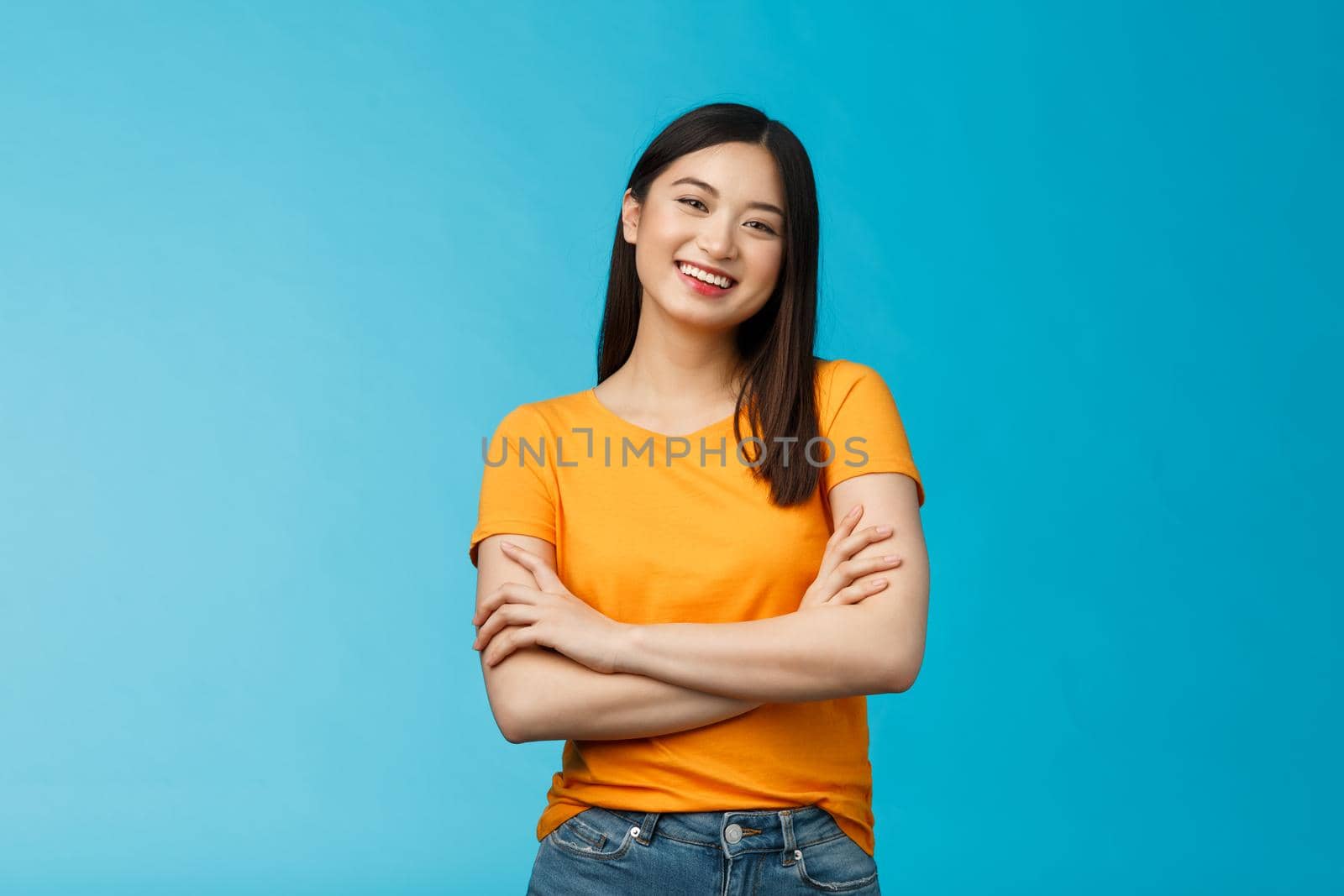 Cheerful friendly asian woman with dark short haircut smiling broadly enthusiastic conversation, talking you casually, cross arms chest confident pose, laughing carefree, stand blue background.