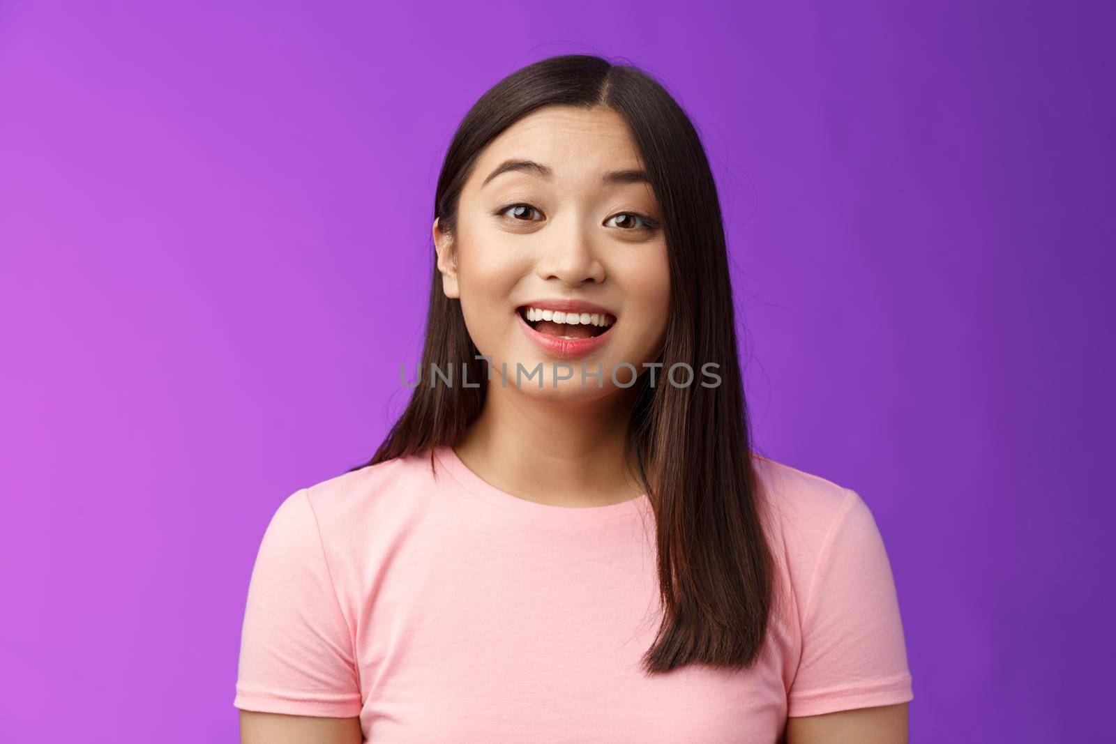 Surprised fascianted cute asian young female raise eyebrows wondered watching amused incredible performance, smiling broadly, happy attend interesting event, stand purple background.