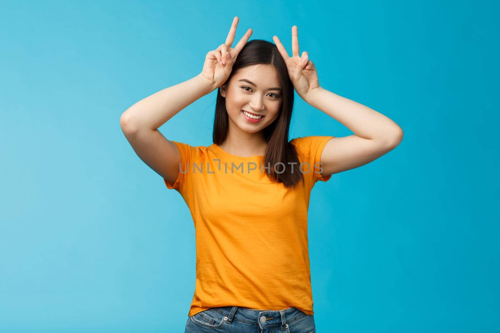 Cute tender asian girlfriend act silly lovely smile, tilt head show playfully ears hold peace victory signs on head, grinning toothy, express joy happiness and delight, stand blue background.