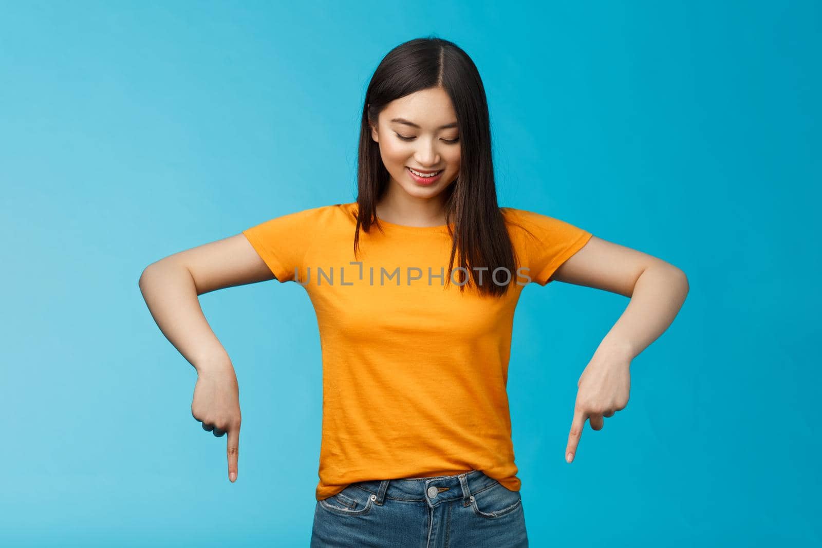 Cute tender feminine asian girl dark haircut look pointing down contemplating interesting product, stare curiously smiling amused, express enthusiasm interest try-out cool thing, blue background by Benzoix