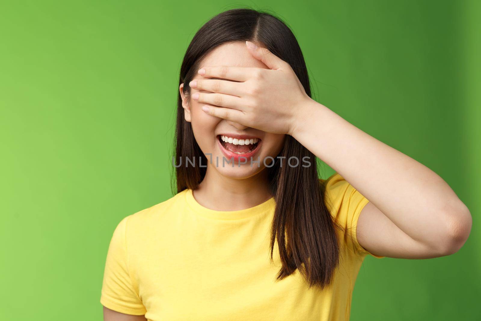 Lively joyful friendly-looking asian girl shut eyes palm, laughing happily, standing amused anticiapting b-day gift, counting ten, playing hide-n-seek, stand green background entertained by Benzoix