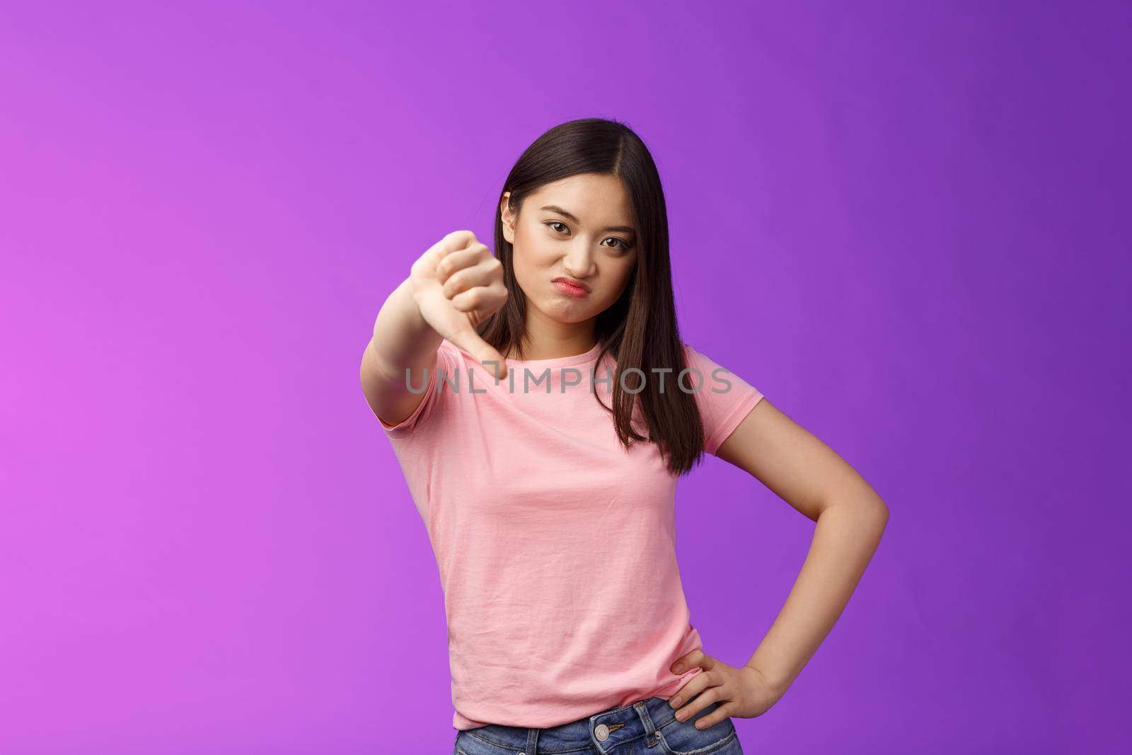 Lame, very bad. Displeased judgemental asian girl show thumb down, grimacing, cringing from disappointmend, unsatisfied awful uninteresting performance, complain, stand purple background.