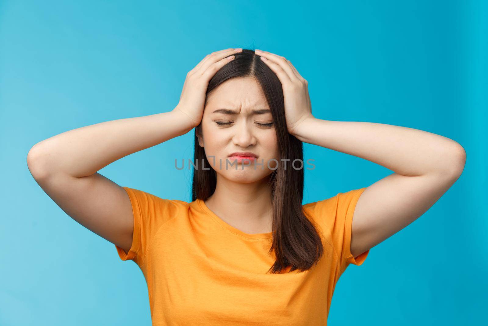 Close-up perplexed upset cute asian girl tired, exhausted piled up work, whining complain tough day, grab head troubled, distressed, close eyes grimacing bothered, stand blue background.
