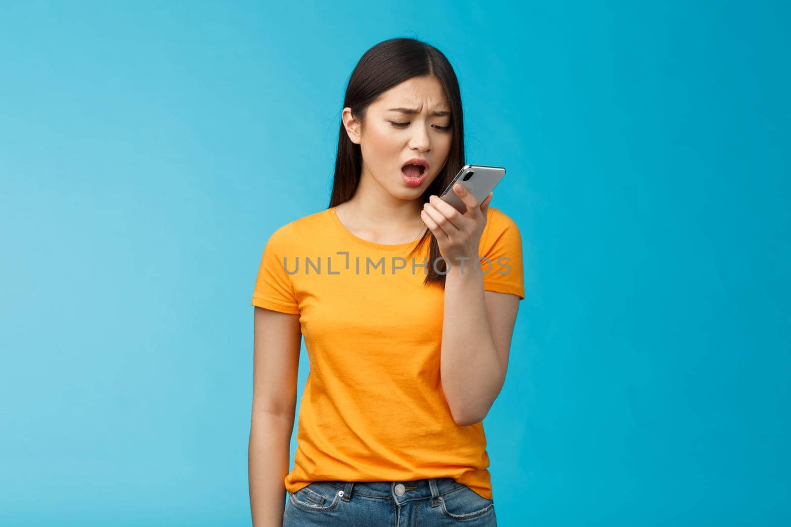 Upset whining displeased moody girlfriend complaining talk into smartphone hold phone near mouth upset, frowning bothered bad connection, record voice message, blue background. Copy space