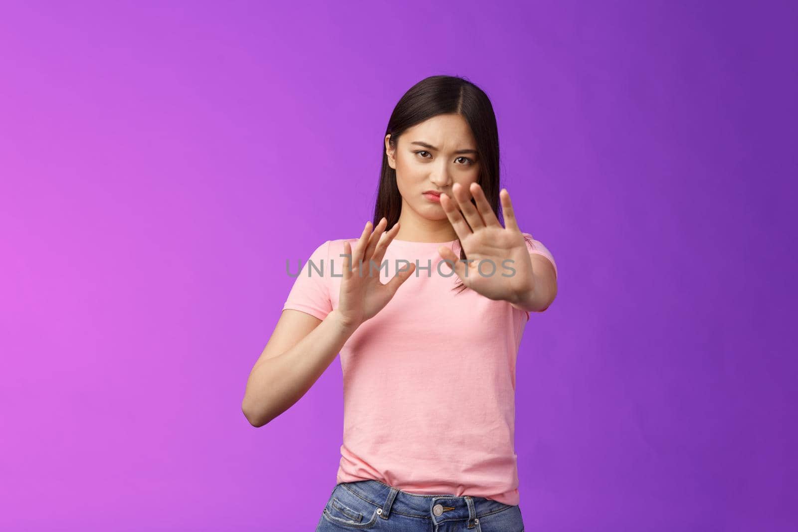 Displeased intense reluctant asian girl blocking, trying protect face, raise hands stop, prohibition gesture, frowning sulking, refusing bothering offer, stand purple background, rejecting.