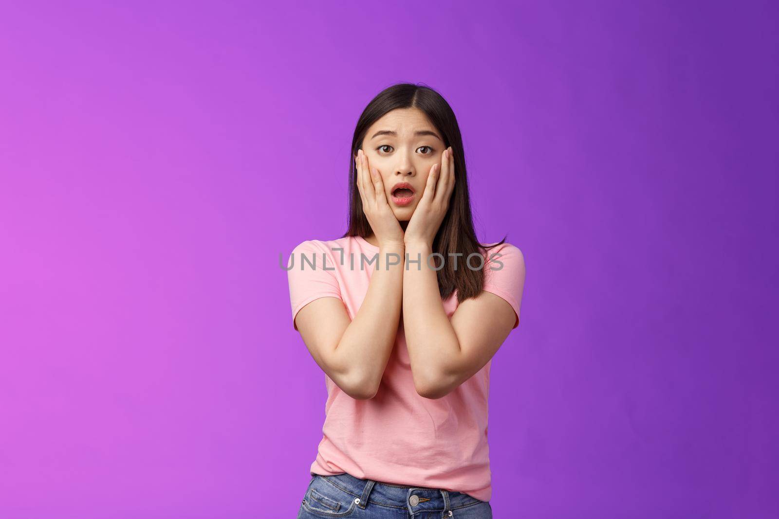 Concerned shocked timid insecure asian woman, feel pitty, shame hearing shocking news, grab face sorry for friend, gasping, opened mouth upset, sighing distressed, stand purple background.
