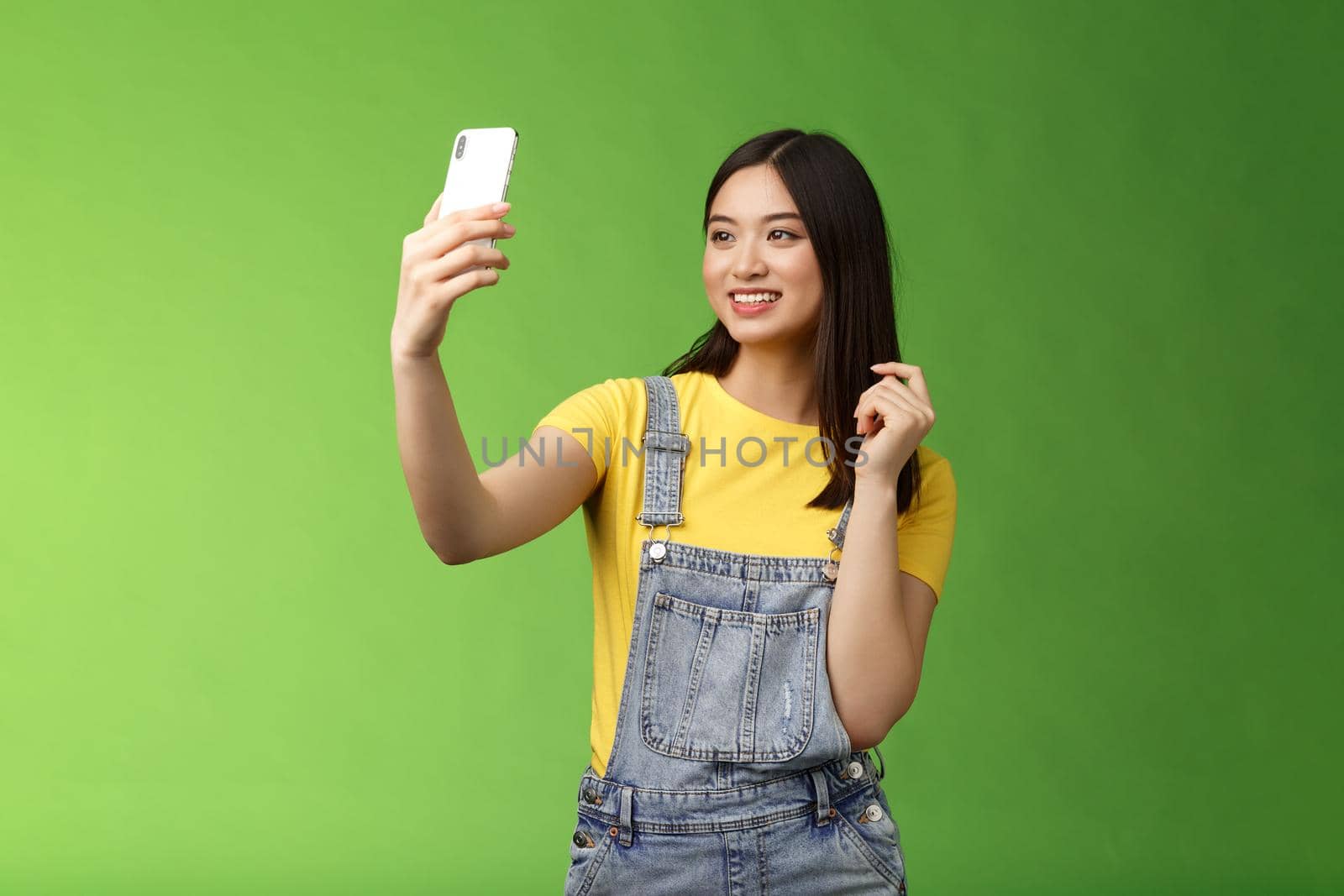 Glamour tender teenage asian female taking selfie, checking haircut, look smartphone front camera, photographing, record video message post online, smiling lovely, green background.