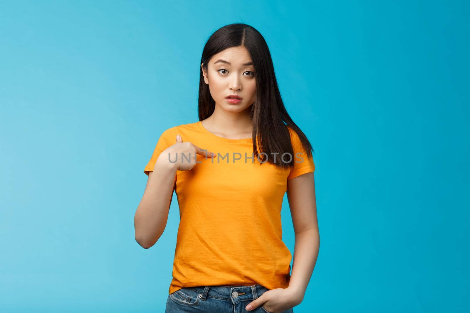 Surprised cute asian urban female student pointing herself look questioned, full disbelief cannot understand, hear own name, look clueless, unsure standing blue background astonished by Benzoix