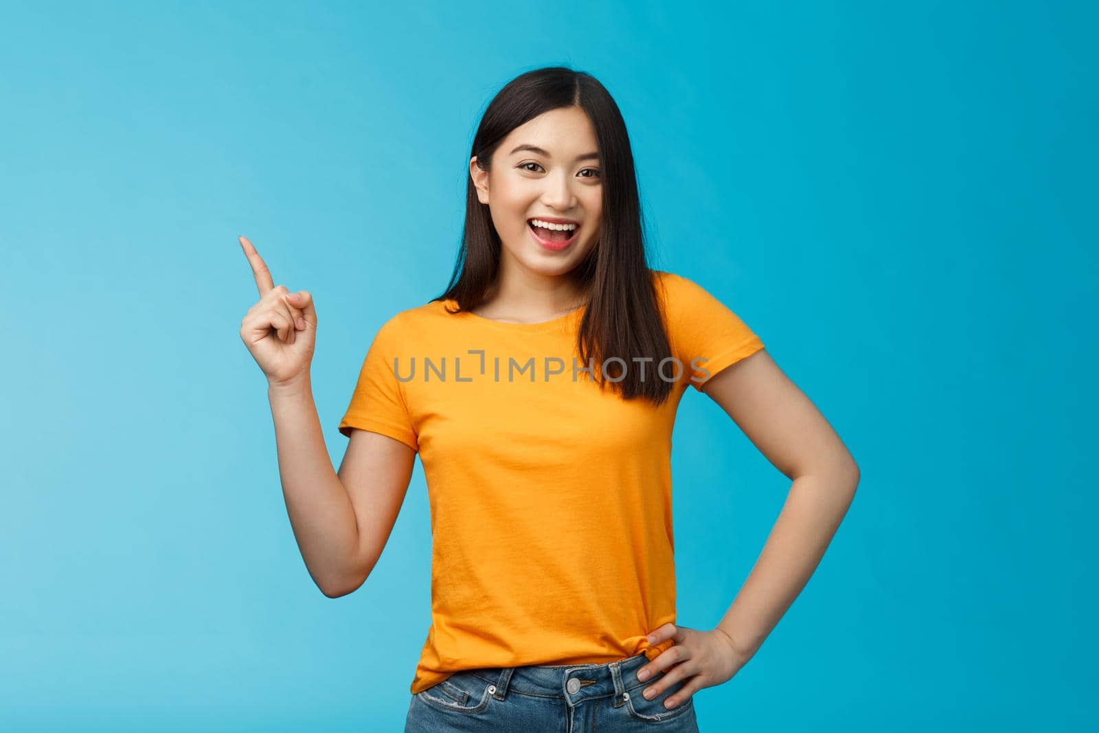 Lively cute friendly-looking asian girl with dark short hair showing way pointing upper left corner and grinning delighted, giving direction, introduce new product, smiling upbeat satisfied.