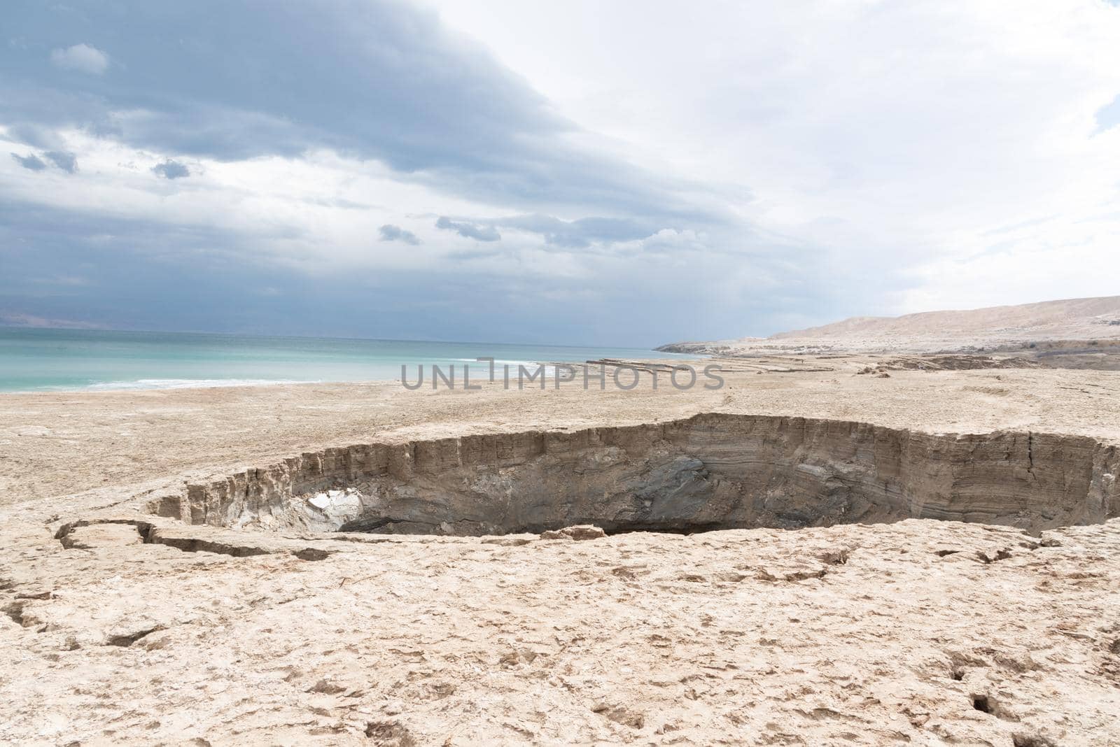 Sinkhole filled with turquoise water, near Dead Sea coastline. Hole formed when underground salt is dissolved by freshwater intrusion, due to continuing sea-level drop. . High quality photo