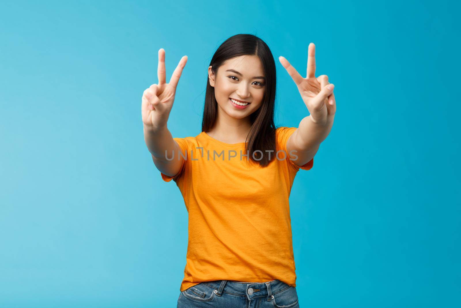 Positive upbeat cute asian girl believe win, aim success extend hands show victory, peace sign smiling broadly, have happy enthusiastic mood, spend carefree vacation travel abroad value pacifism.