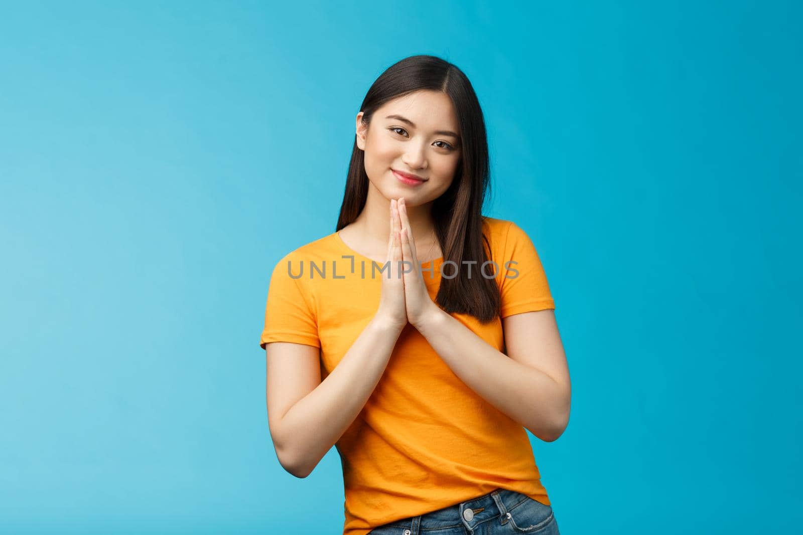 Pretty please girl asking politely. Cute charming asian woman smiling tenderly, hold hands pray grinning begging for favour, plead, look thankful for help stand blue background joyful, caring.