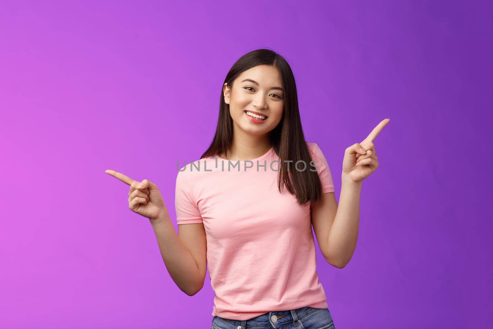 Charismatic relaxed cute asian woman short haircut pointing sideways introduce variety choices, showing left and right products, smiling joyfully, easily making decision, stand purple background.