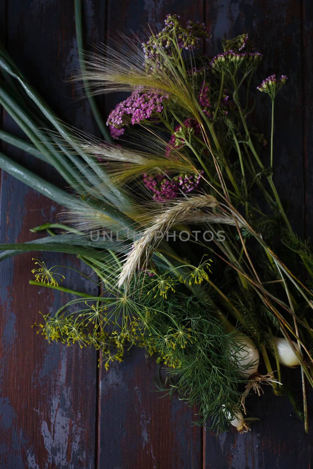 Fresh green onion, dill flowers, rye spikelets and yarrow pink flowers on dark blue table, summer concept, flat lay, selective focus