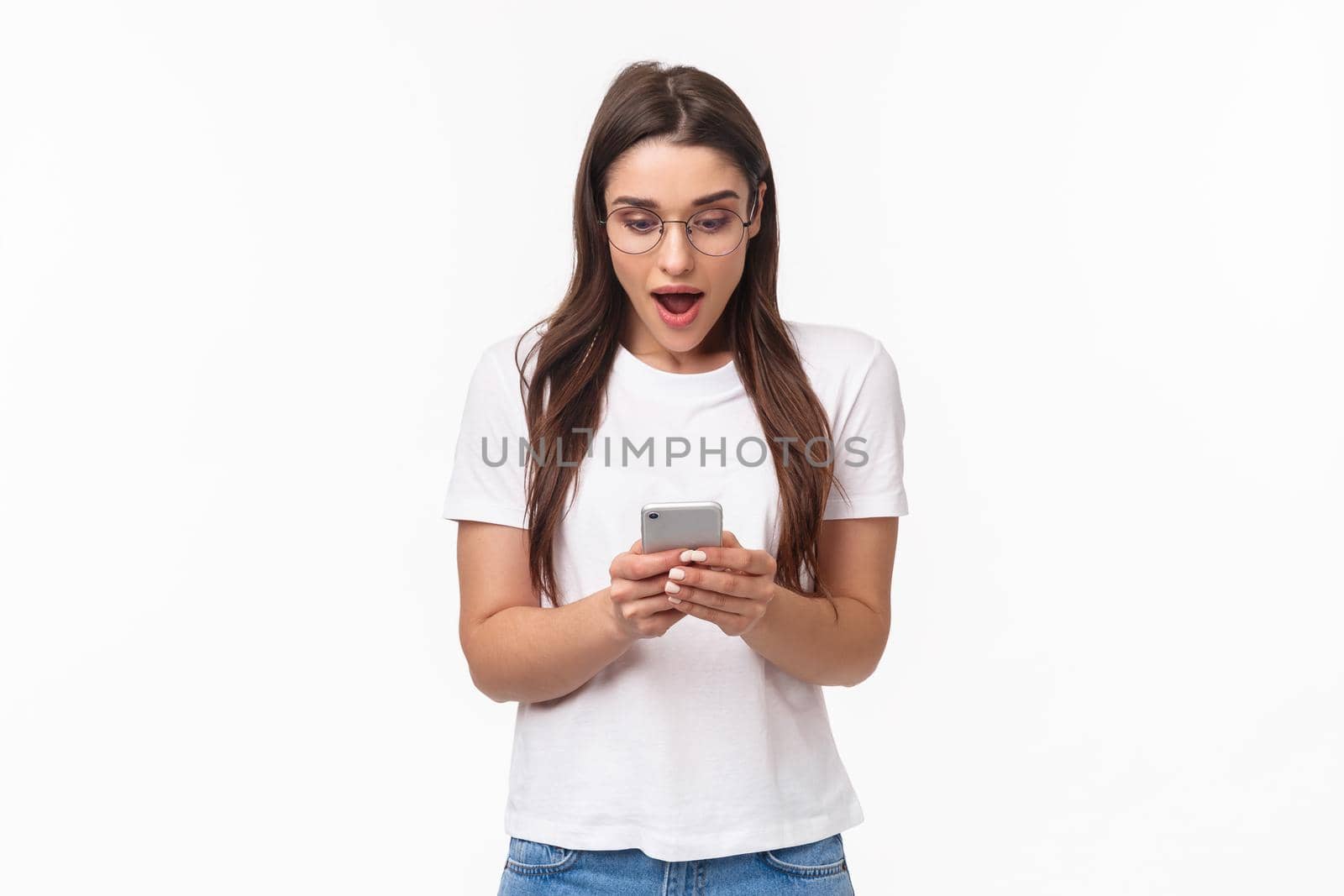Communication, technology and lifestyle concept. Portrait of surprised and amazed, excited young caucasian woman in glasses, looking at mobile phone, receive awesome new via text message.