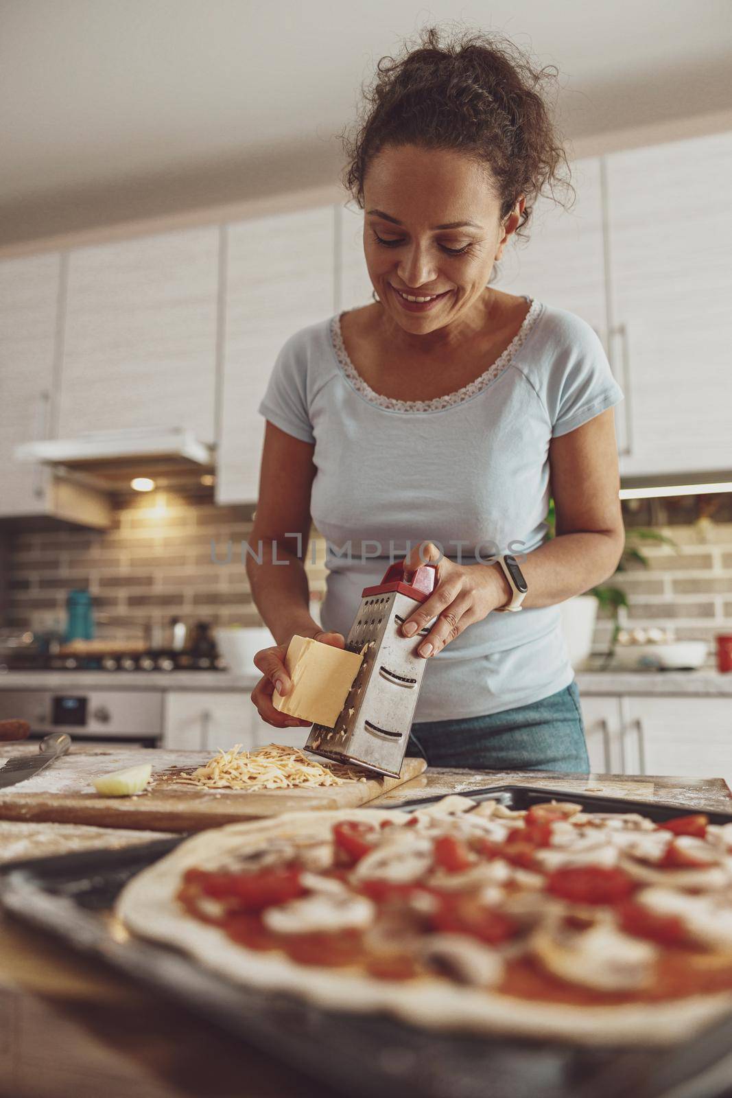 Cooking pizza with mushrooms and cheese by a young woman at home in the kitchen