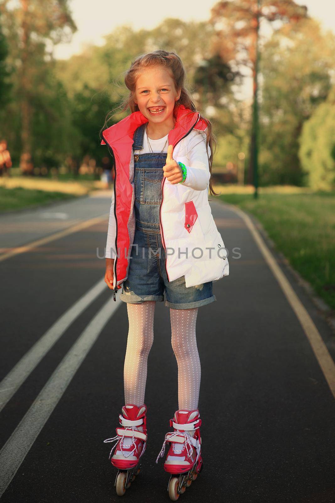 happy little girl on roller skates makes a gesture thumb up in t by SmartPhotoLab