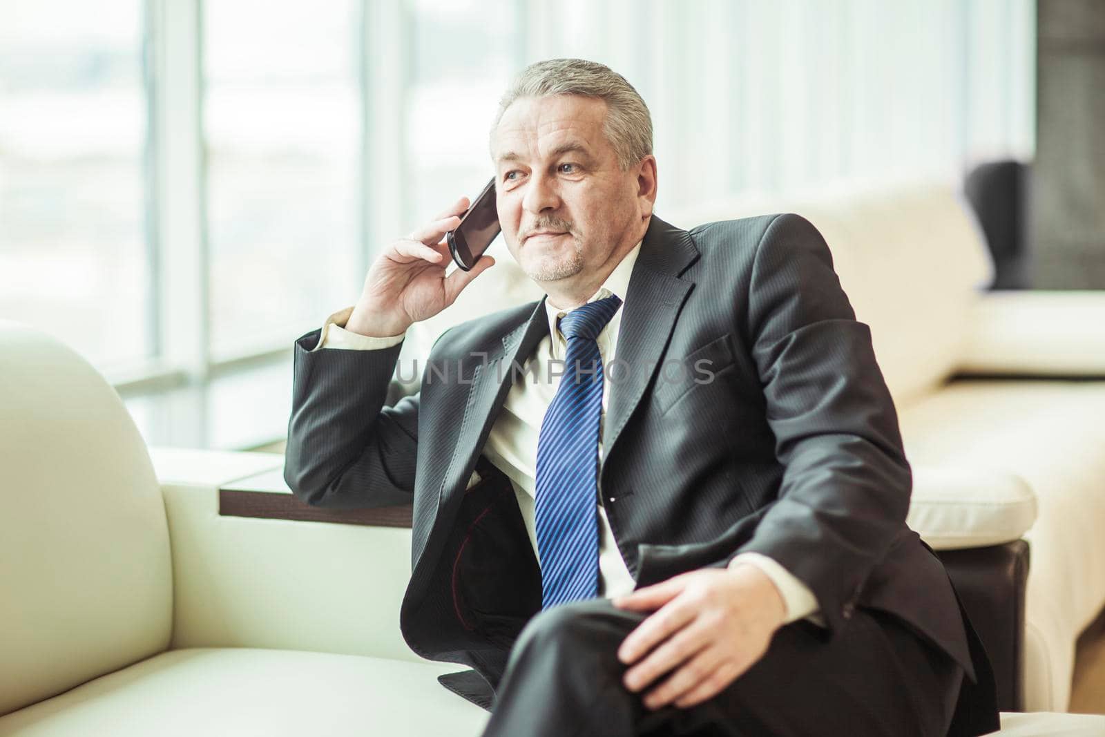 experienced businessman talking on smartphone sitting on couch in the office.