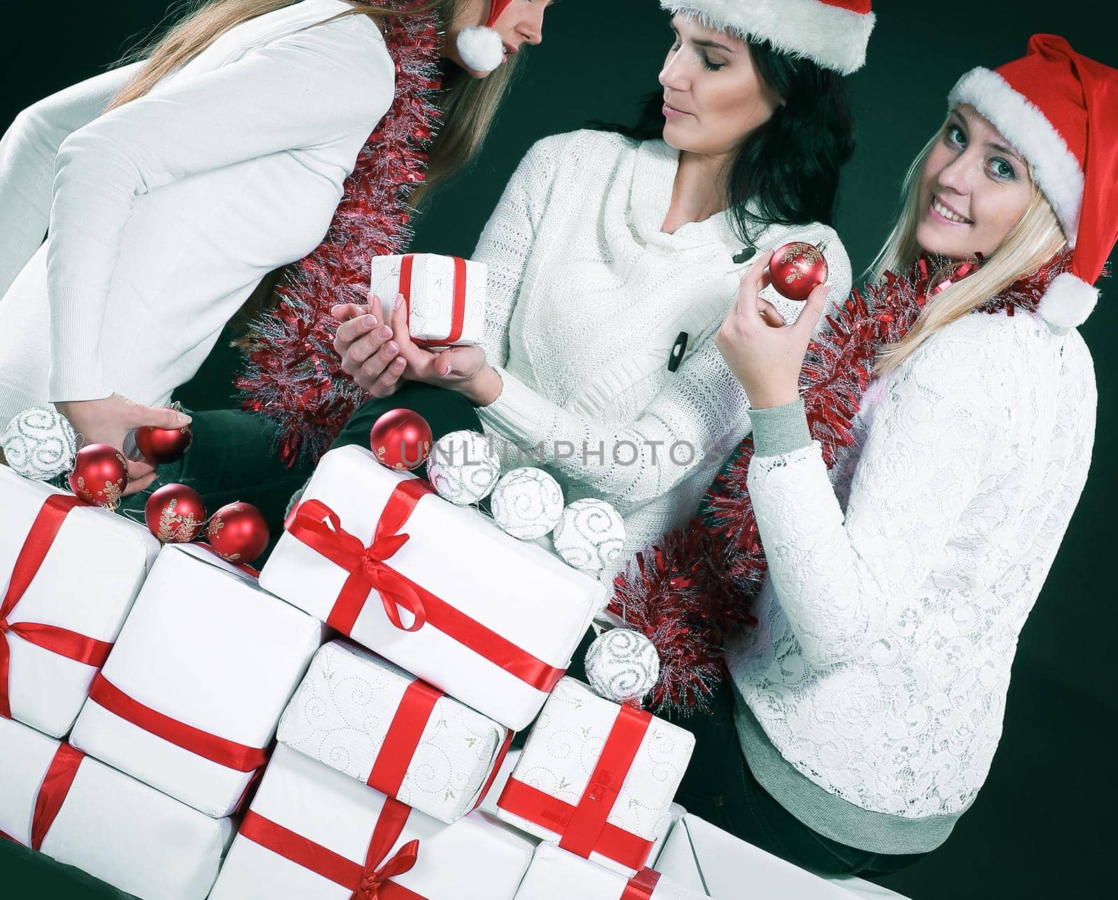 three happythree happy young girls dressed as Santa Claus sitting with a bunch of Christmas gifts. isolated on black