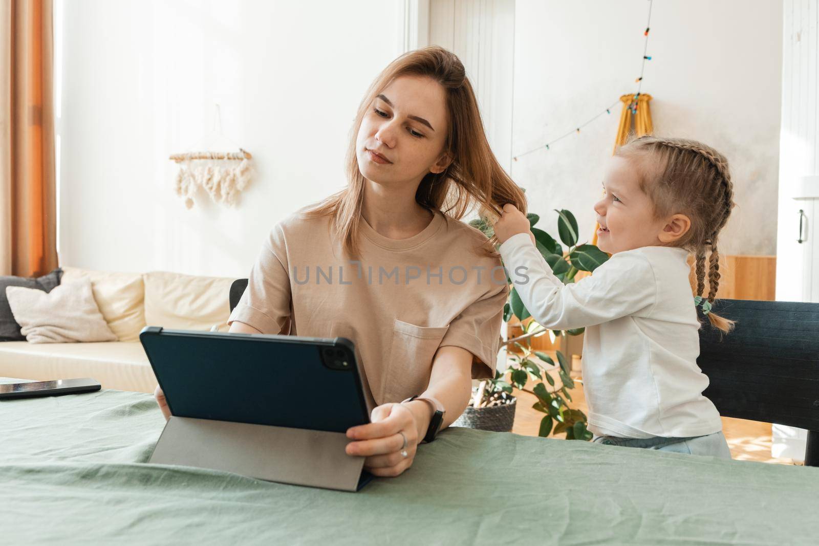 Daughter interferes with a young woman working from home on a tablet. Freelance work