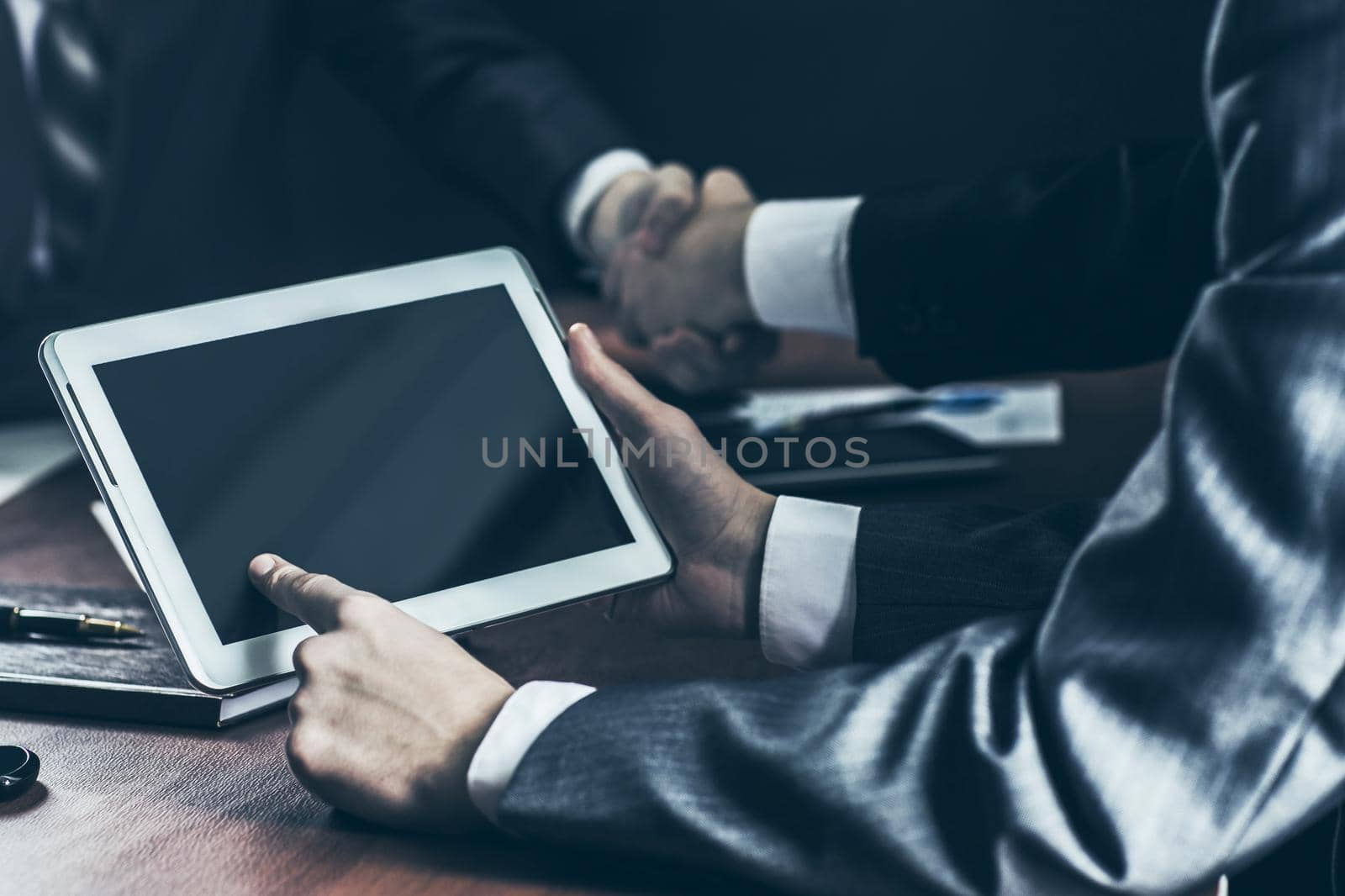 closeup of businessman with digital tablet in the background of handshake of business partners. by SmartPhotoLab