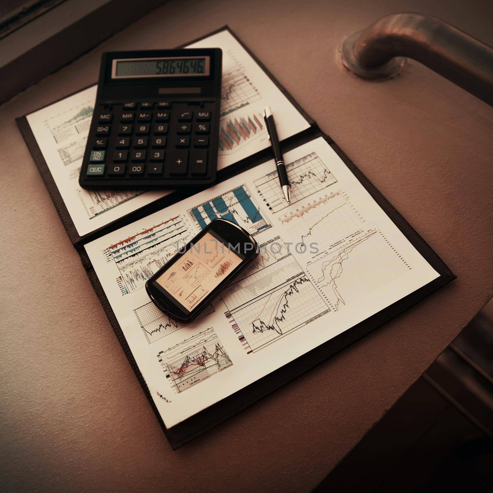 A folder with the charts of financial analysis. Diagrams in the phone's screen, next is calculator and pen on the table