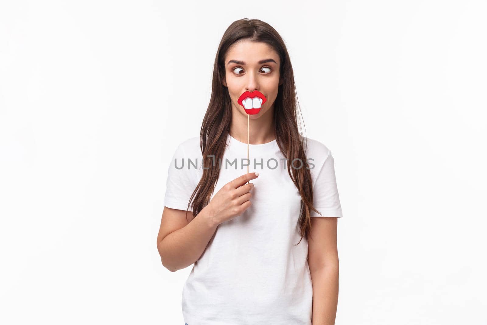 Entertainment, fun and holidays concept. Portrait of funny and joyful celebrating fools day april first, having fun, holding stick with lips and big teeth, show hilarious grimaces, white background by Benzoix