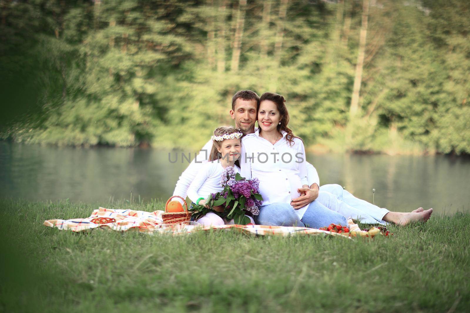 father,pregnant mother and little daughter on a picnic near the river.the photo has a empty space for your text