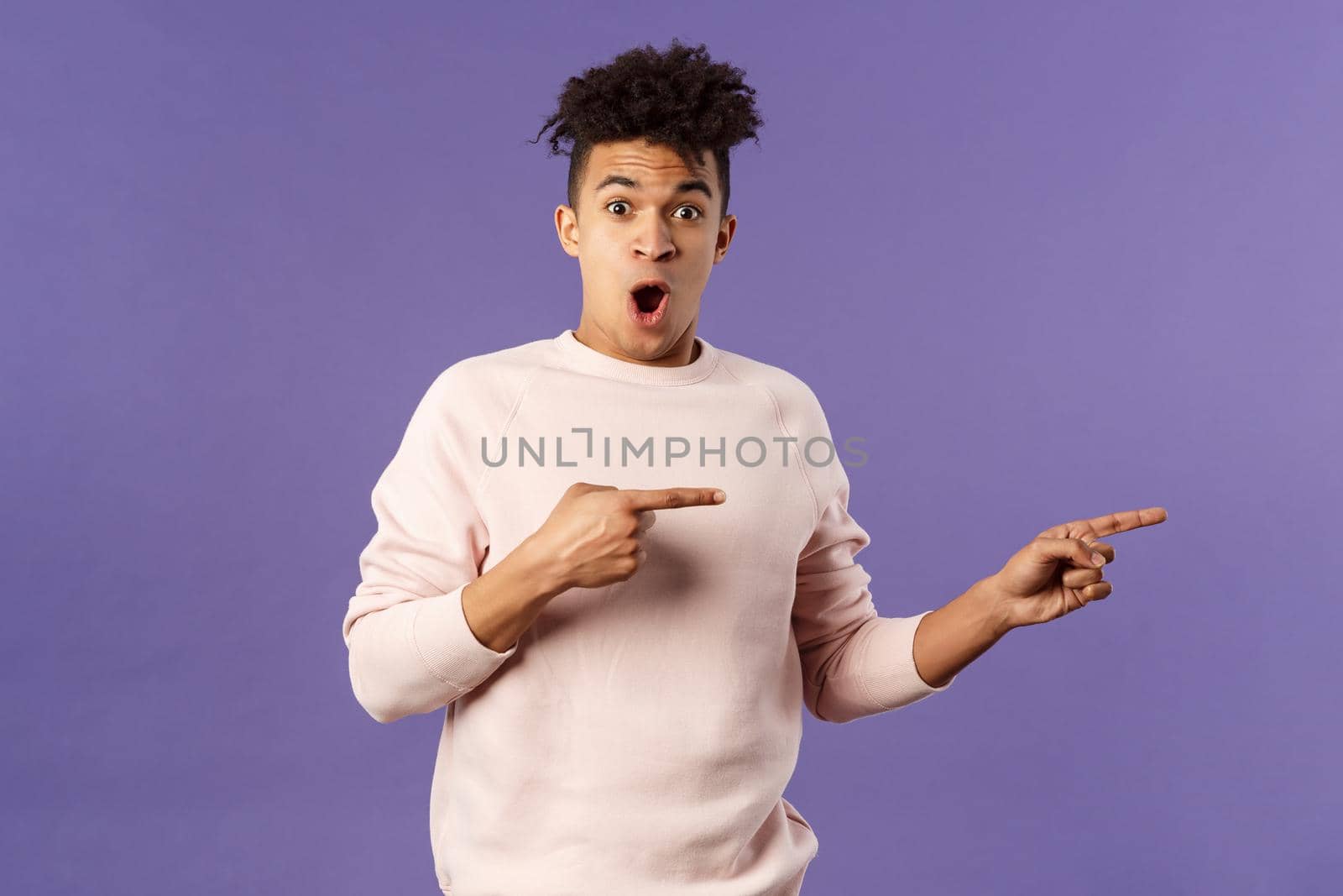 Portrait of excited, handsome young hispanic man talking about amazing party going nearby, describe incredible deal, open mouth wondered, pointing fingers right, recommend buy or download.