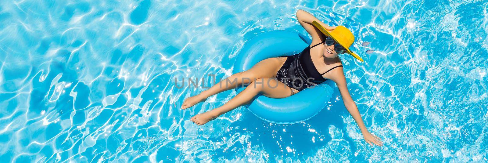 Woman sitting in a swimming pool on a ring pool float in a large yellow sunhat. BANNER, LONG FORMAT