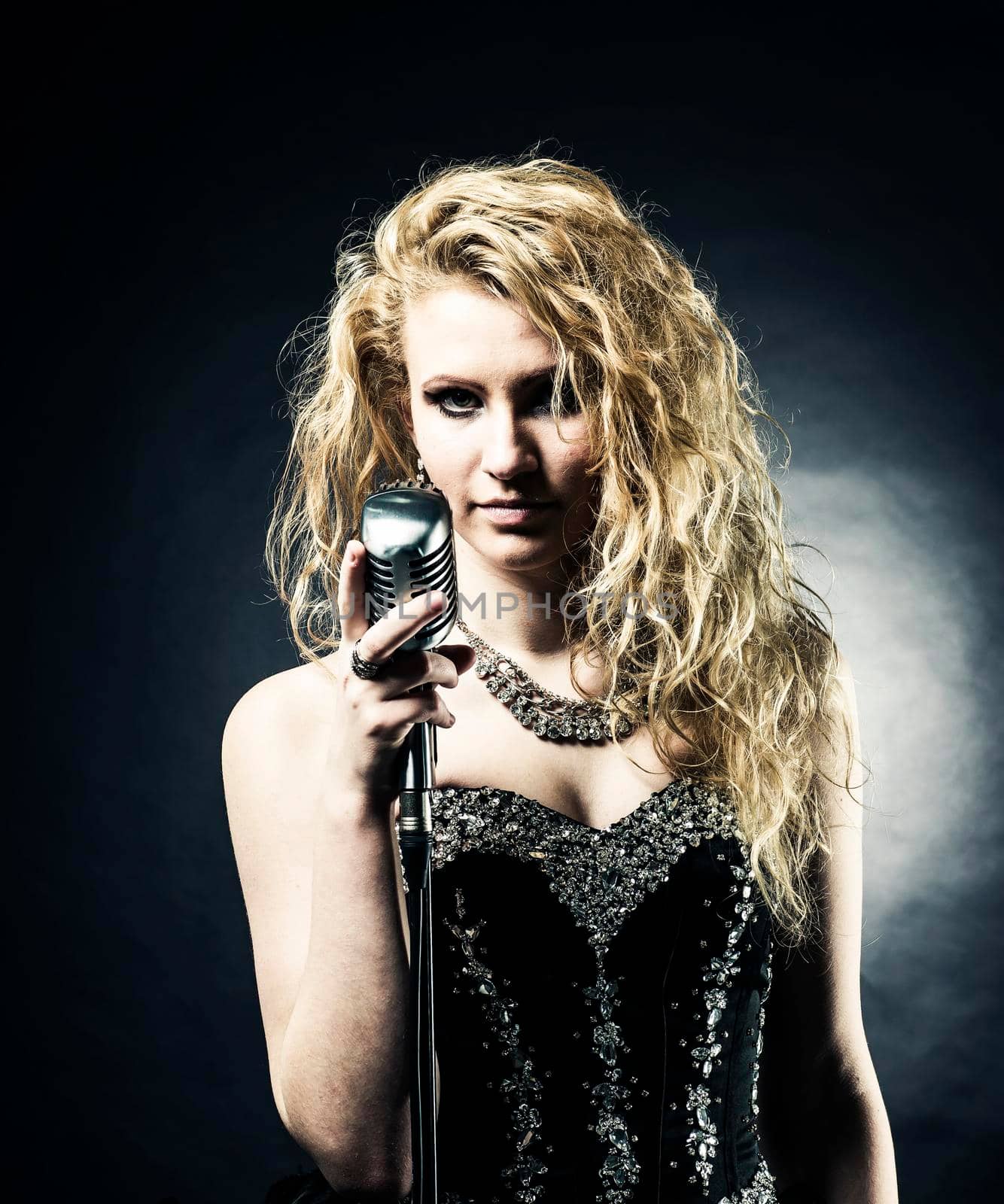 beautiful blonde woman singer in a black dress holding a microphone and sings a song.photo on dark background
