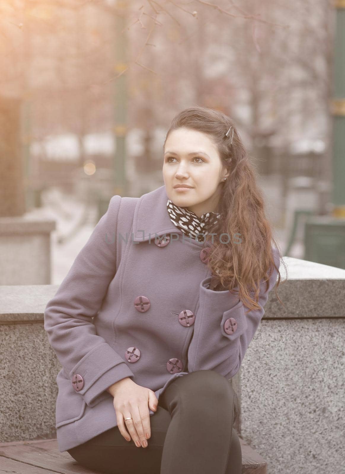 woman in fashionable coat sitting on bench in city.