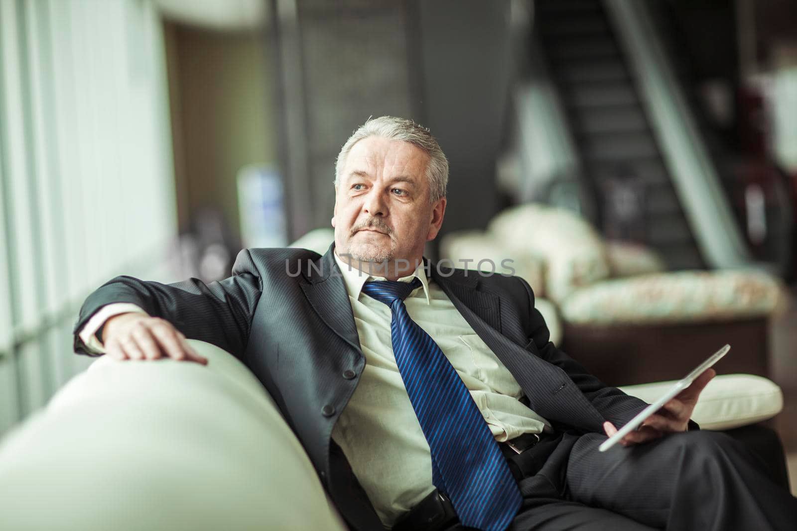 successful businessman with digital tablet sitting on the sofa in the private office by SmartPhotoLab