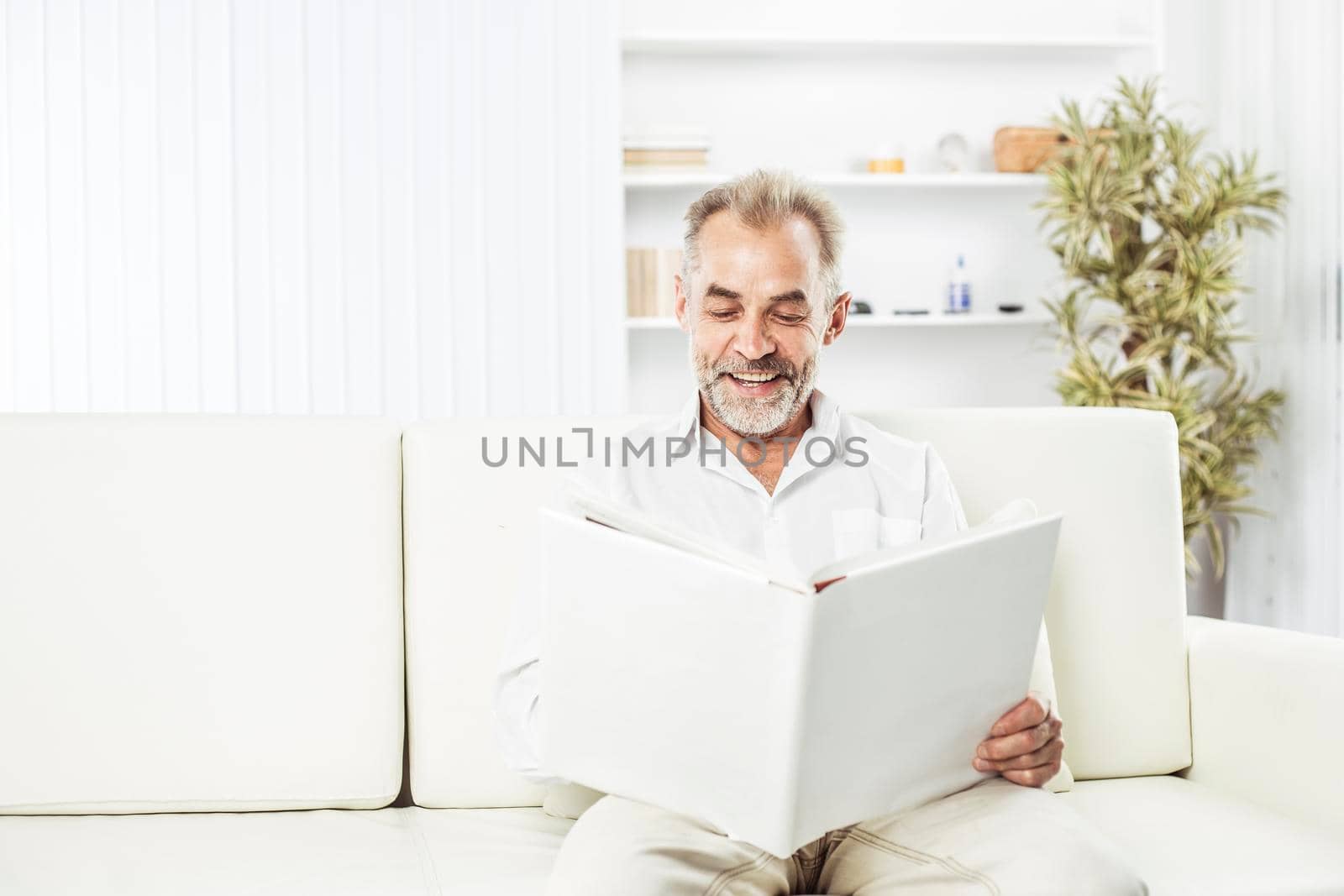 businessman with a magazine sitting on sofa in bright office. the photo has a empty space for your text