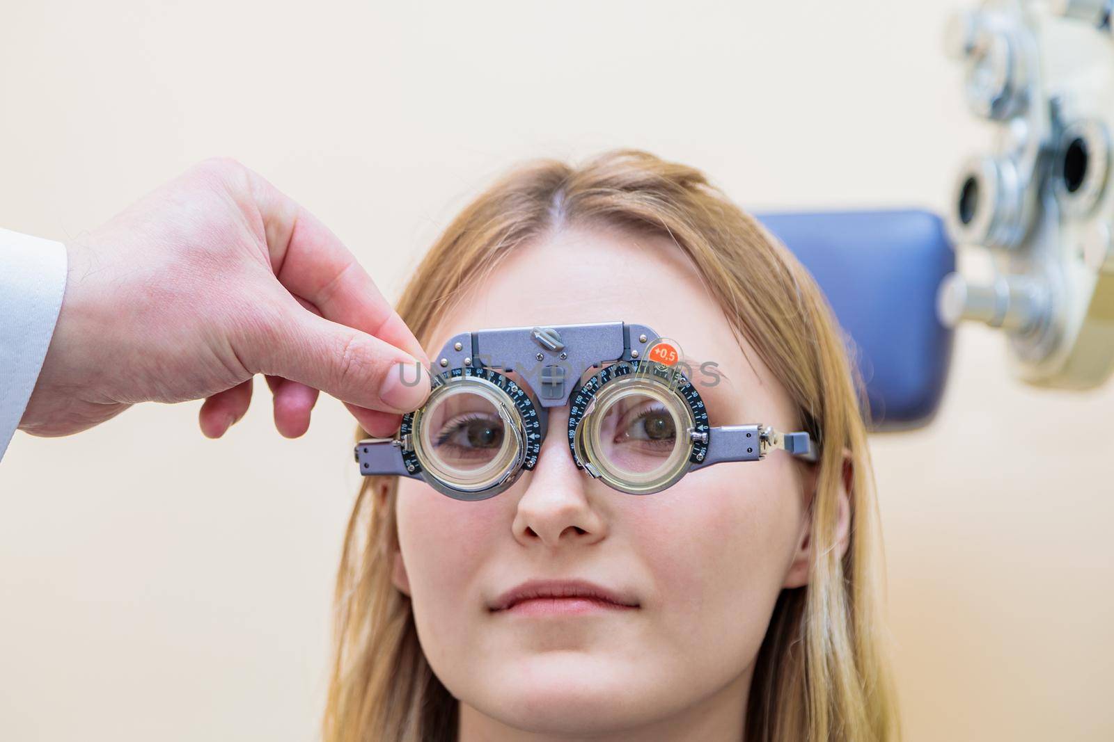 A male optometrist checks the eyesight of a young girl with a trial frame.
