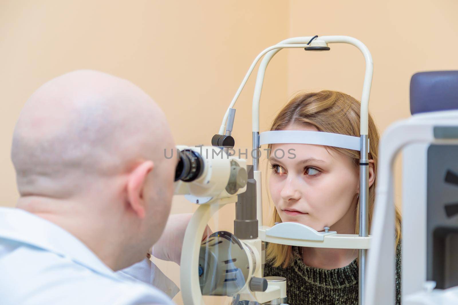 A male ophthalmologist checks the eyesight of a young girl using a modern device with a light beam.