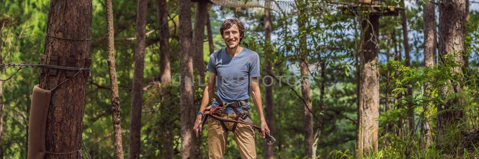 Young attractive man in adventure rope park in safety equipment. BANNER, LONG FORMAT