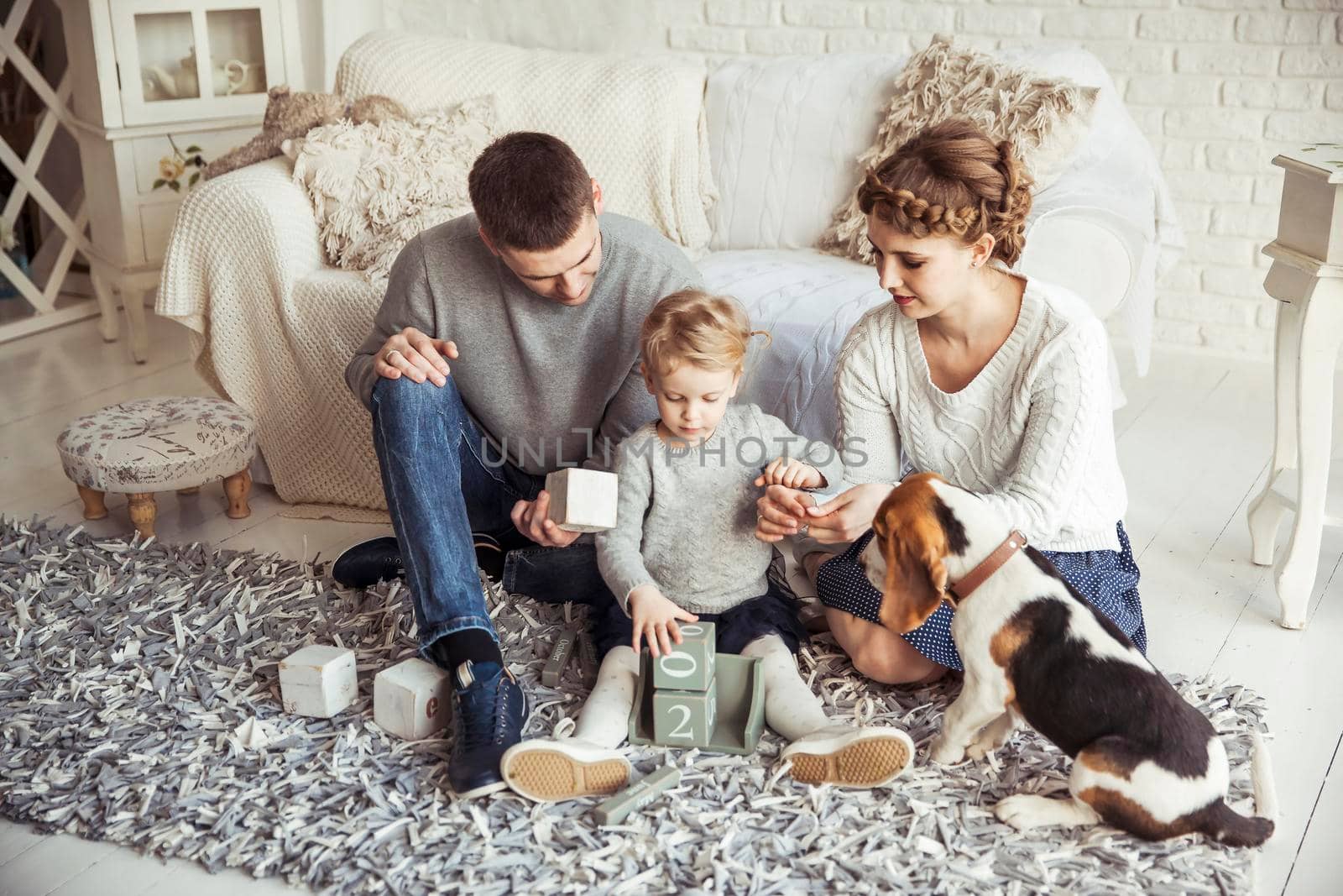happy parents and five year old daughter playing with a pet dog in the spacious living room on Sunday