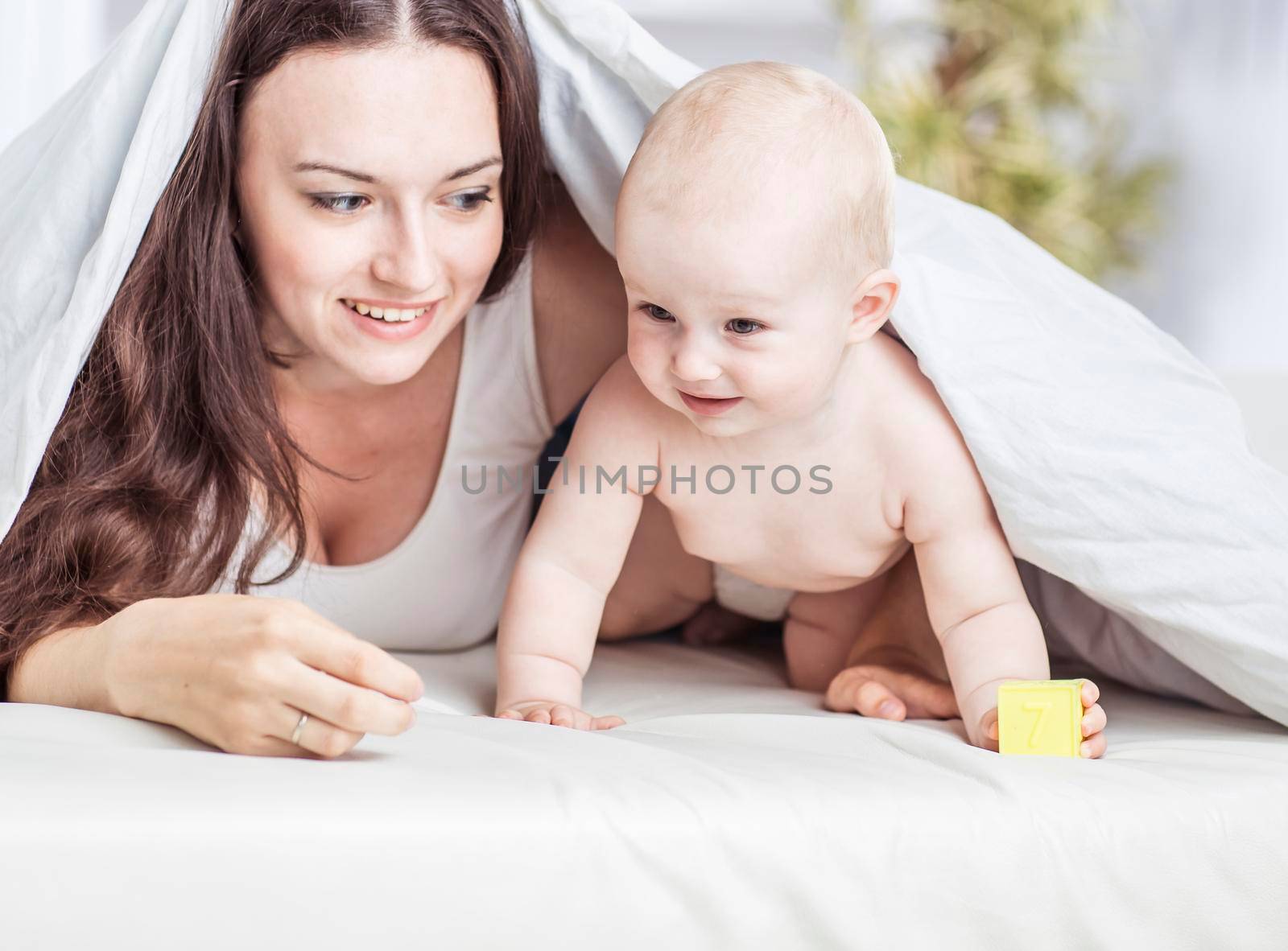 concept of happy mothers: happy mother and her year-old child playing on the sofa in the bedroom by SmartPhotoLab