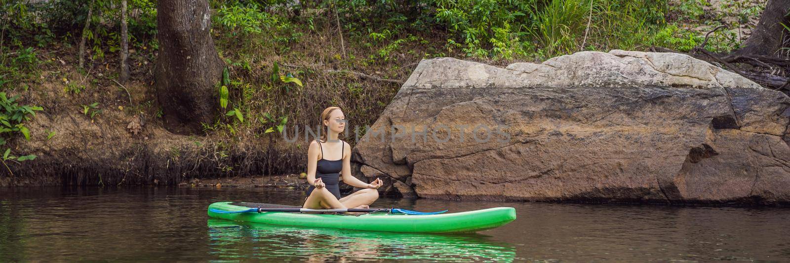 Sporty woman in yoga position on paddleboard, doing yoga on sup board, exercise for flexibility and stretching of muscles. BANNER, LONG FORMAT