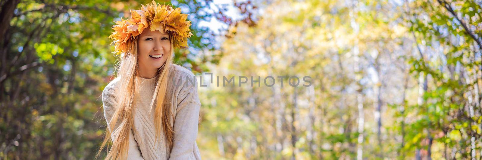 Outdoors lifestyle close up portrait of charming blonde young woman wearing a wreath of autumn leaves. Smiling, walking on the autumn park. Wearing stylish knitted pullover. Wreath of maple leaves. BANNER, LONG FORMAT