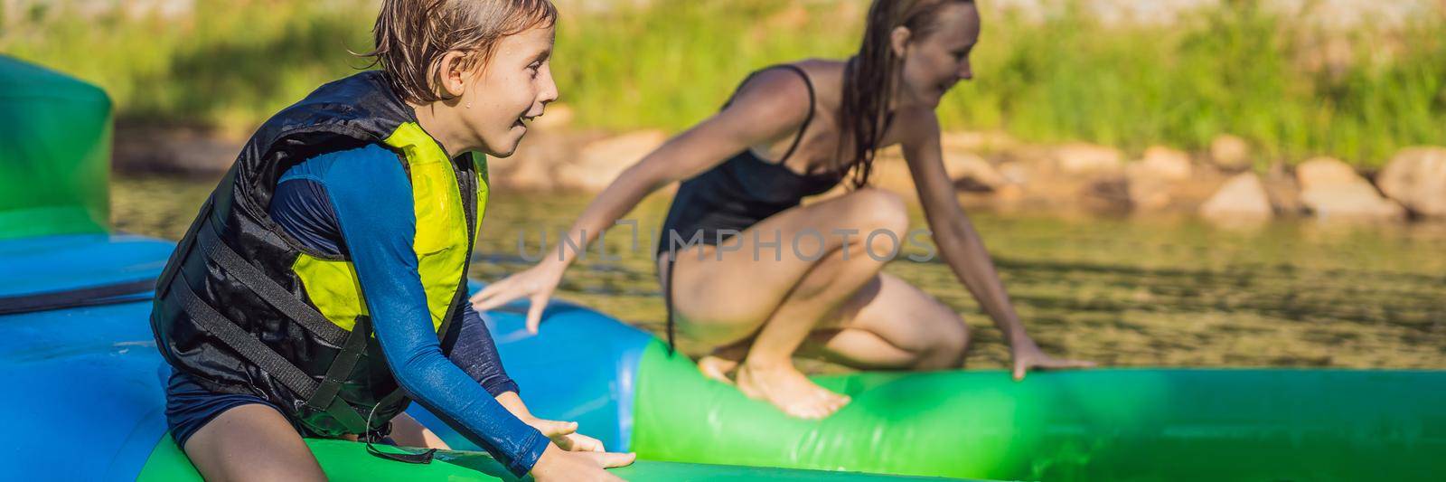 Mother and son go through an inflatable obstacle course in the pool. BANNER, LONG FORMAT