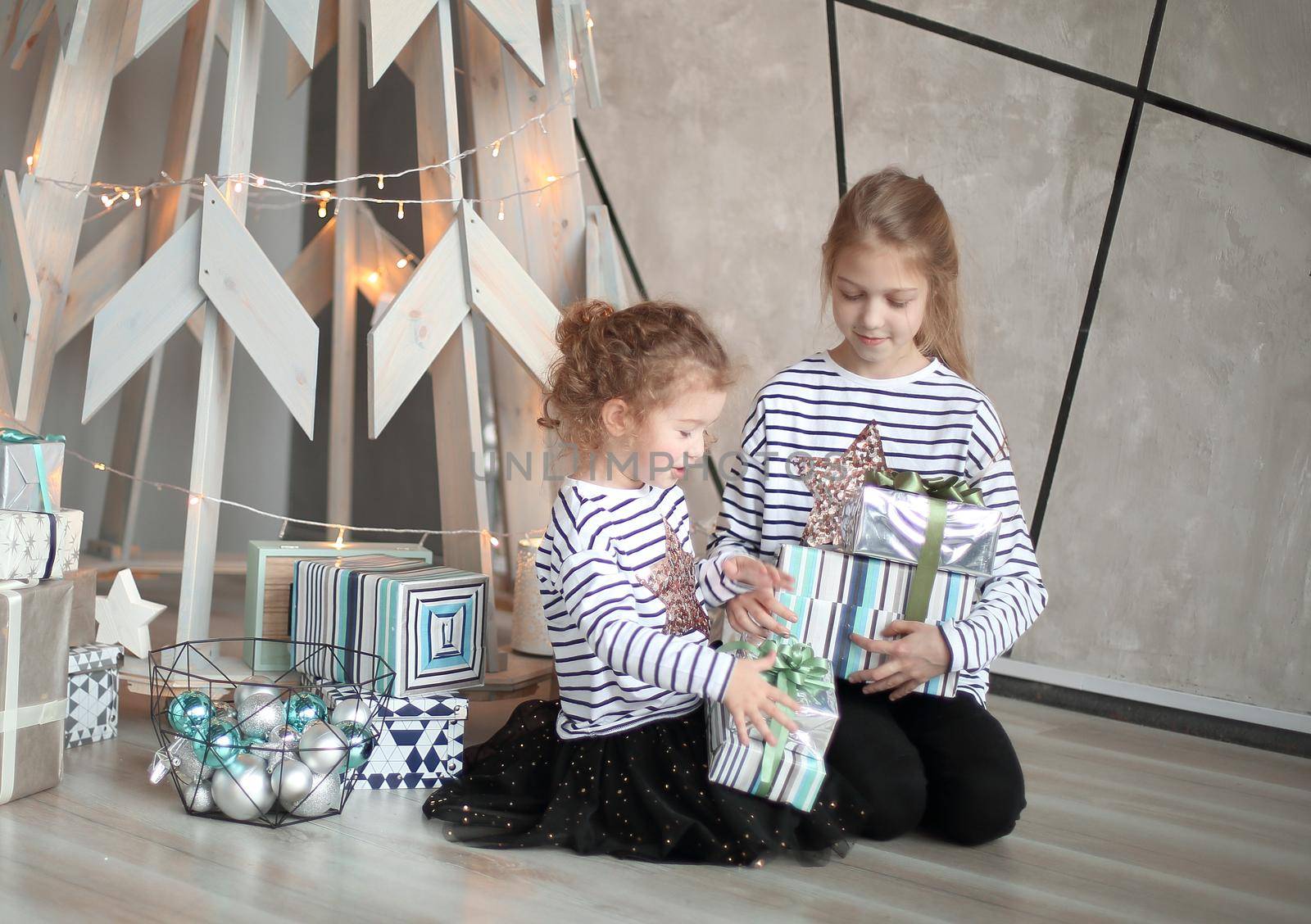 two little sisters sitting near a stylized Christmas tree. the concept of a family holiday