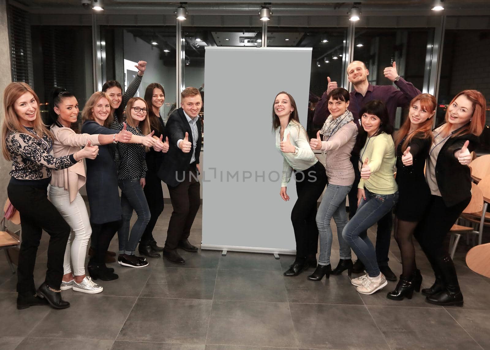business team standing in front of a large banner and showing thumb up by SmartPhotoLab