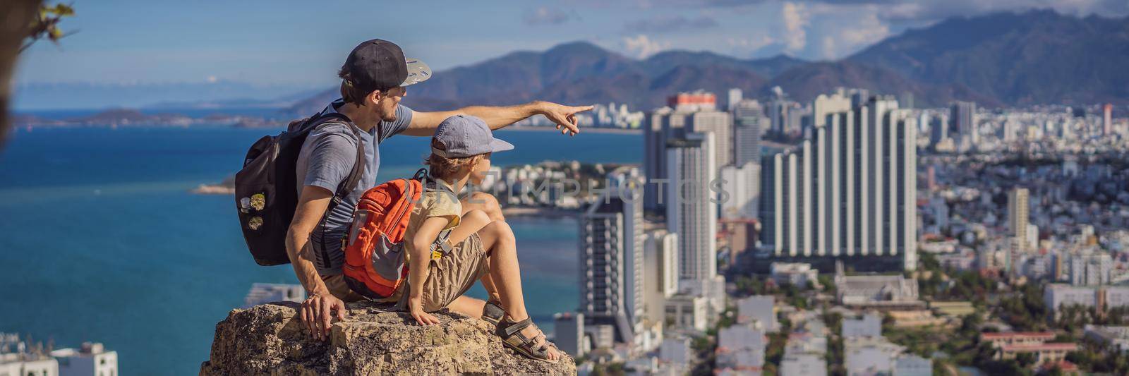 Father and son local tourist sits on a rock and enjoys the view of her city. Local tourism concept. Tourism after COVID 19 BANNER, LONG FORMAT by galitskaya