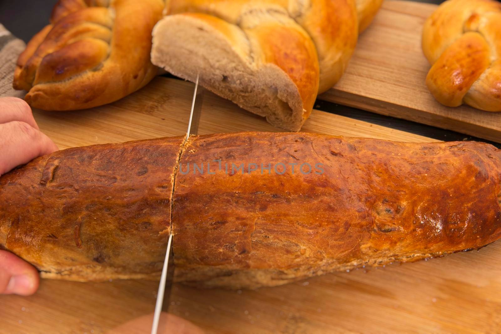 A person with a knife slicing a bread loaf. Bread in the shape of a braid. Sweet Challah. Slice of banana bread for breakfast, side view. Cherry tomatoes . High quality photo