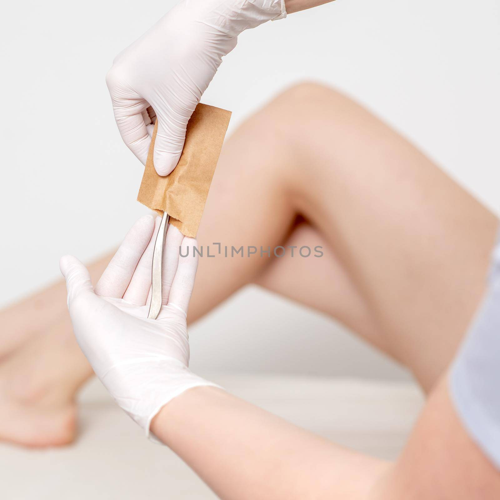 Human hands in protective gloves taking off medical or beauty tools from craft envelope before procedures on background of female legs