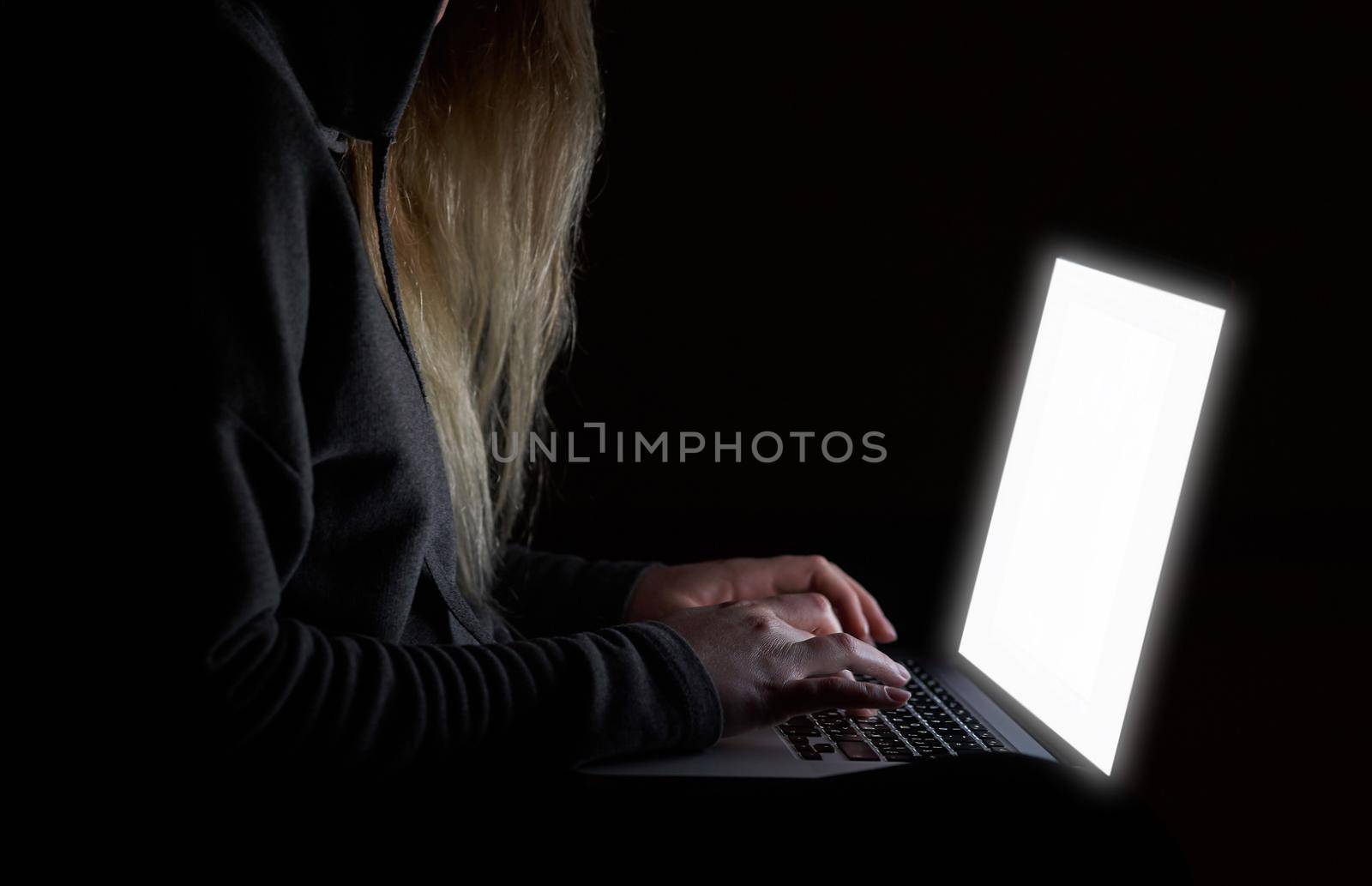 Overhead hacker in the hood working with laptop and mobile phone typing text in the darkroom. Russian hacker hacking the server in the dark. A hacker girl sitting in the dark with her laptop