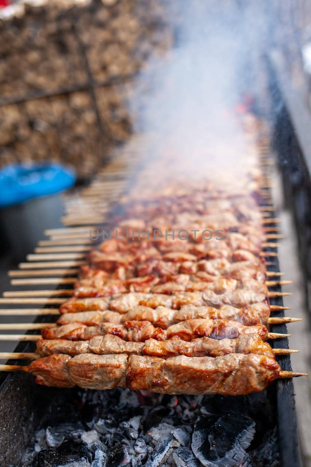 A lot of juicy meat kebabs in a row on the grill. Meat pieces strung on wooden skewers on the grill. The process of cooking kebabs with a lot of smoke. Cooking in nature