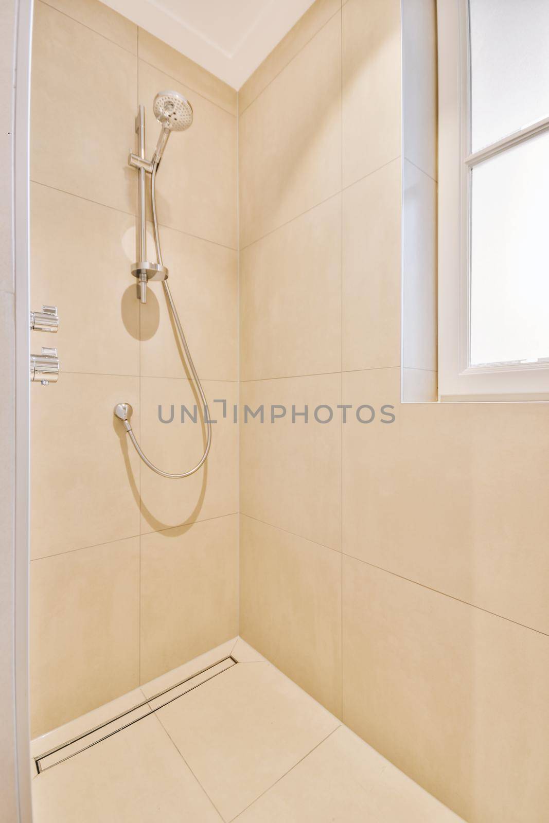 Shower faucets attached to tiled wall near glass partition and ornamental curtail in washroom at home